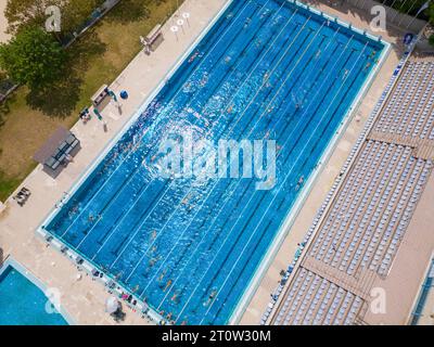 Der offene Sportpool glitzerte unter der hellen Sonne, während die Menschen in seinem einladenden Wasser schwimmen. Ihre synchronisierten Züge erzeugten ein lebendiges t Stockfoto