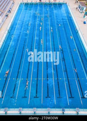 Der offene Sportpool glitzerte unter der hellen Sonne, während die Menschen in seinem einladenden Wasser schwimmen. Ihre synchronisierten Züge erzeugten ein lebendiges t Stockfoto