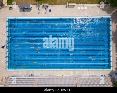 Der offene Sportpool glitzerte unter der hellen Sonne, während die Menschen in seinem einladenden Wasser schwimmen. Ihre synchronisierten Züge erzeugten ein lebendiges t Stockfoto