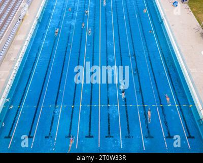 Der offene Sportpool glitzerte unter der hellen Sonne, während die Menschen in seinem einladenden Wasser schwimmen. Ihre synchronisierten Züge erzeugten ein lebendiges t Stockfoto