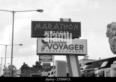 Marathon Rent a Car Business und Rhodes Voyager Reisebüro Schild, das Touristen über die Lage des Geschäfts in Schwarz-weiß informiert Stockfoto