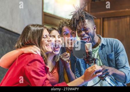 Eine vielfältige Gruppe junger Männer und Frauen, die inbrünstig um ein Kondensatormikrofon singen und ihre Begeisterung und musikalische Leidenschaft zum Ausdruck bringen. Stockfoto
