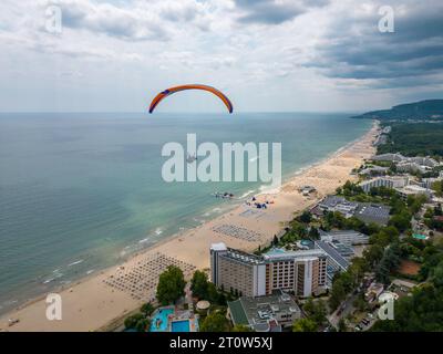 Ein Gleitschirmflieger schwingt über das Meer und den Wald mit einem atemberaubenden Blick auf den Ferienort Albena in Bulgarien und schafft ein unvergessliches Erlebnis. Stockfoto