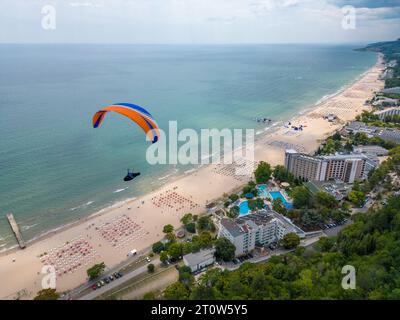 Ein Gleitschirmflieger schwingt über das Meer und den Wald mit einem atemberaubenden Blick auf den Ferienort Albena in Bulgarien und schafft ein unvergessliches Erlebnis. Stockfoto