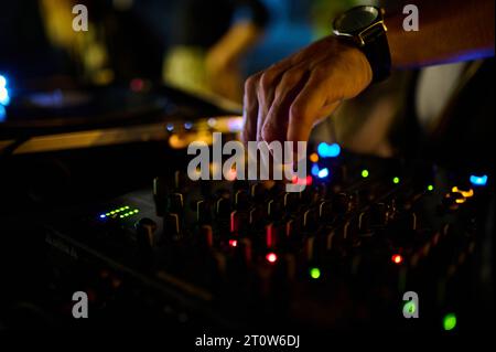 Eine Nahaufnahme der Hand des DJs auf der Mixer-Konsole in einem Nachtclub, bei der Musik- und Tanzatmosphäre gebastelt wird. Stockfoto