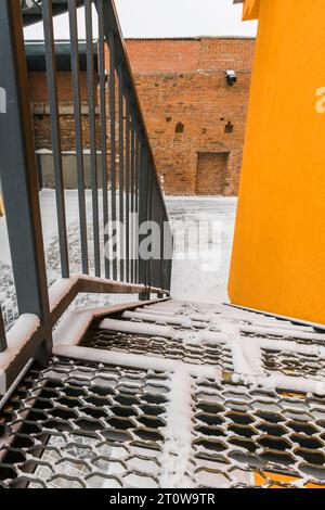 Notausstiegstreppe des großen Fabrikgebäudes im Winter mit Schnee. Treppenstufe aus verzinktem Metall. Stockfoto