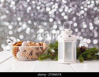 Schöne Neujahrs- und Weihnachtskomposition mit einer weißen Laterne, einem Korb mit glasiertem Lebkuchen und getrockneten Orangenscheiben. Fichtenzweige. , Bokeh. Stockfoto