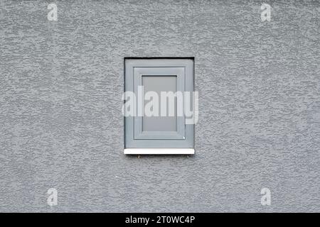 Kleines PVC-Fenster in Grau auf einer grauen strukturierten Wand. Platz für Kopierraum oder Text. Stockfoto