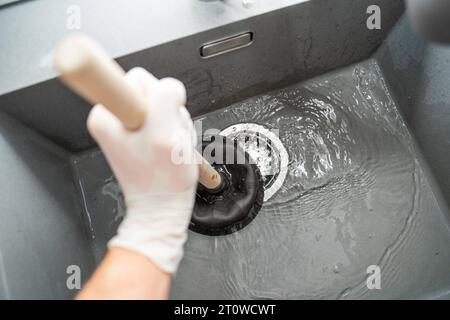 Augsburg, Bayern, Deutschland. September 2023. Handwerker versucht eine Verstopfung in einem Waschbecken mit einer Saugglocke zu lösen *** Handwerker versucht eine Verstopfung in einem Waschbecken mit einer Saugglocke zu lösen Credit: Imago/Alamy Live News Stockfoto