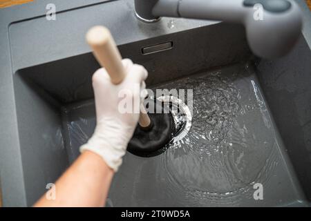 Augsburg, Bayern, Deutschland. September 2023. Handwerker versucht eine Verstopfung in einem Waschbecken mit einer Saugglocke zu lösen *** Handwerker versucht eine Verstopfung in einem Waschbecken mit einer Saugglocke zu lösen Credit: Imago/Alamy Live News Stockfoto