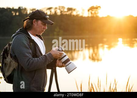 Landschaftsfotograf und Tierfotograf schaut sich Fotos auf dem Kamerabildschirm an, die er bei Sonnenuntergang am See gemacht hat Stockfoto