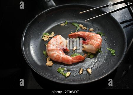 Zwei Riesengarnelen werden in Olivenöl mit Knoblauch und Kräutern in einer schwarzen Pfanne frittiert, um eine Gourmet-Meeresfrüchte-Mahlzeit mit frischen Krebstieren zuzubereiten, Copy Spa Stockfoto