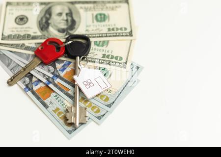 Zwei Schlüssel liegen auf verstreuten US-Dollar-Scheinen. Das Konzept des Immobilienkaufens, der Hypothek, des Immobilienkaufens. Stockfoto