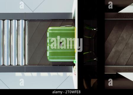 Ein grüner Koffer, der auf einem Förderband in einen Flughafenscanner eindringt. Sicherheitsprüfung Stockfoto