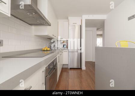 Apartment mit Küche mit weißen Möbeln, integrierten Edelstahlgeräten, kleiner Insel auf einer Seite Stockfoto