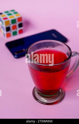 Foto von rotem Getränk, blauem Smartphone und Rubik auf rosa Hintergrund Stockfoto