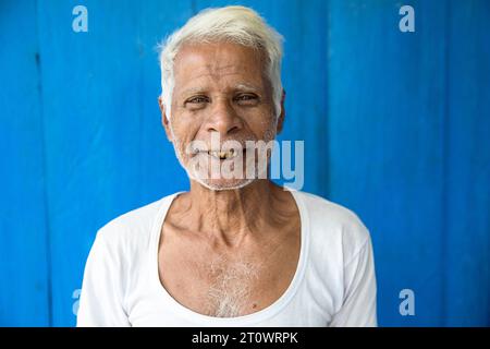 Ein einheimischer Mann lächelt vor einer blauen Holzwand in seinem Haus in einem kleinen Dorf auf der Insel Majuli, Brahmaputra River, Assam, Indien Stockfoto
