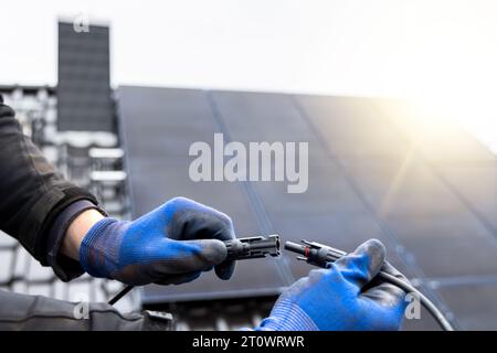 Hände, die die Anschlusskabel des Solarmoduls auf einem Dach eines Hauses halten Stockfoto