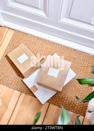 Stapel der gelieferten Papppakete auf einer Türmatte neben dem Eingang der Wohnung Stockfoto