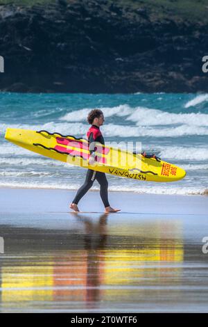 Ein RNLI-Rettungsschwimmer mit einem Vanquish Life Saving Surfbrett und einem Spaziergang zum Meer am Fistral Beach in Newquay in Cornwall, Großbritannien. Stockfoto