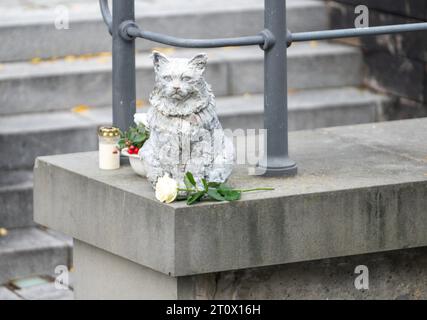 Memmingen, Deutschland. Oktober 2023. Ein Denkmal für die berühmte Katze Chicco der Stadt befindet sich auf einer Mauer am Stadtbach. Die burmesische Katze war in der schwäbischen Stadt bekannt und sehr beliebt. Anfang 2023 starb Chicco. Als Ergebnis wurden Spenden gesammelt und die Memmingener Künstlerin Cornelia Brader fertigte eine Bronzeskulptur der Katze, um an ihn zu erinnern. Quelle: Stefan Puchner/dpa/Alamy Live News Stockfoto