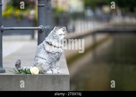 Memmingen, Deutschland. Oktober 2023. Ein Denkmal für die berühmte Katze Chicco der Stadt befindet sich auf einer Mauer am Stadtbach. Die burmesische Katze war in der schwäbischen Stadt bekannt und sehr beliebt. Anfang 2023 starb Chicco. Als Ergebnis wurden Spenden gesammelt und die Memmingener Künstlerin Cornelia Brader fertigte eine Bronzeskulptur der Katze, um an ihn zu erinnern. Quelle: Stefan Puchner/dpa/Alamy Live News Stockfoto