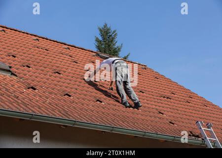 Ein unbekannter Mann bereitet das Dach für die Installation von Solarpaneelen vor, rote Taschen auf dem Dach des Hauses, bereit für Photovoltaik-Anlagen Stockfoto