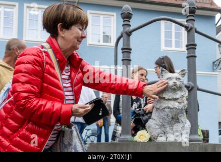 Memmingen, Deutschland. Oktober 2023. Brigitte Heckenrath streichelt das Denkmal der berühmten Katze Chicco. Die burmesische Katze war in der schwäbischen Stadt bekannt und sehr beliebt. Anfang 2023 starb Chicco. Als Ergebnis wurden Spenden gesammelt und die Memminger-Künstlerin Cornelia Brader fertigte eine Bronzeskulptur der Katze an, um an ihn zu erinnern. Quelle: Stefan Puchner/dpa/Alamy Live News Stockfoto