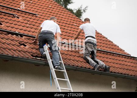 Die Arbeiter bereiten das Dach für die Installation von Solarpaneelen vor. Zwei Männer auf dem Dach eines Familienhauses. Photovoltaik-Installation Stockfoto