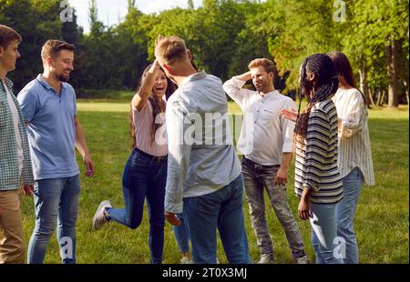 Fröhliche Gruppe von besten Freunden gibt sich gegenseitig hohe fünf, während sie sich im Park treffen. Stockfoto