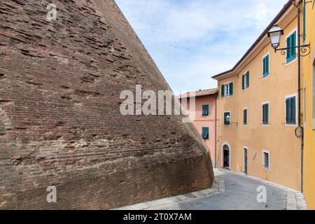 Straße in der Stadt Lari, Italien, gesäumt von historischen Häusern mit verputzten bunten Wänden und der befestigten Backsteinmauer des Schlosses von Lari (Castello de Stockfoto