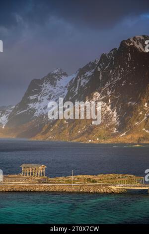 Gestelle für getrockneten Fisch auf Sakrisoy Island, schneebedeckten felsigen Bergen im Rücken, Sakrisoy, reine, Lofoten, Norwegen Stockfoto