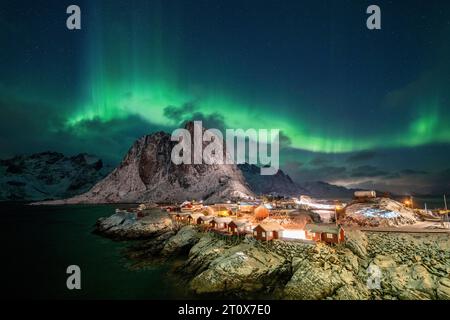 Nordlichter (Aurora Borealis) über Rorbuer-Hütten von Hamnoy, verschneite Berge dahinter, Hamnoy, reine, Moskenesoya, Lofoten, Norwegen Stockfoto