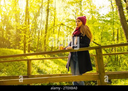 Junger Mann mit schwarzer Jacke, Schal und rotem Wollmütze, der in einem Herbstpark genießt Stockfoto