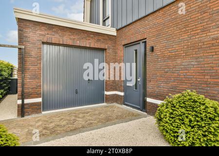 Ein graues Garagentor vor einer roten Backsteinwand mit grünen Büschen und Sträuchern auf beiden Seiten des Gebäudes Stockfoto