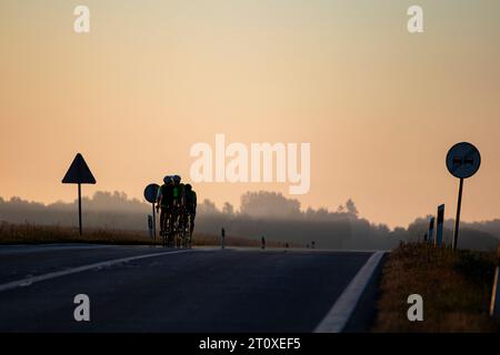 Gruppe von Radfahrern am Morgen Sonnenaufgang auf der Asphaltstraße mit Schildern auf beiden Seiten der Straße Stockfoto