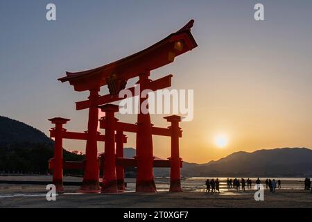 Miyajima, Japan-10. April 2023; Wahrzeichen Shinto-Schrein oder Torii-Tor der Insel Itsukushima, bei Sonnenuntergang bei Ebbe mit Menschen am Strand und Sonnenschein Stockfoto