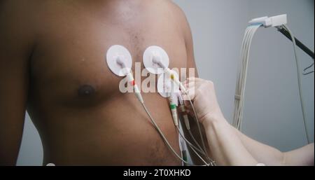 Nahaufnahme eines Kardiologen, der Sensoren zur holter-Überwachung bei Herzkranken einsetzt. Afroamerikaner während der Elektrokardiographie im Kardiologiesaal. Funktionelle Rehabilitation im Krankenhaus. Stockfoto