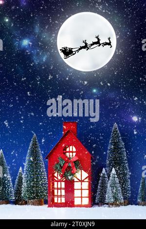Stillleben von rotem Weihnachtsspielzeughaus und Weihnachtsmann-Schlitten über Vollmond. Kreative Weihnachtskomposition mit Weihnachtsklausel. Weihnachtshintergrund. Stockfoto
