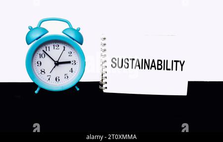 Das Wort nachhaltige Entwicklung steht auf einem Notizblock neben einer Uhr auf weißem und schwarzem Hintergrund. Stockfoto