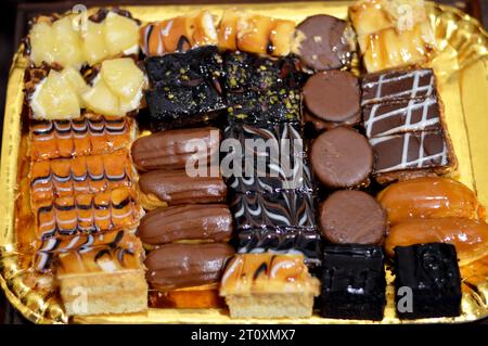 Verschiedene kleine kleine Tortenstücke mit verschiedenen Belägen und gefüllt mit verschiedenen Füllungen, Schwammkuchen mit brauner und weißer Schokolade, Karamell, Marmelade, Stockfoto