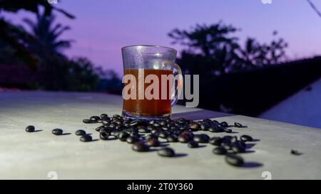 Eine Tasse schwarzen Kaffee in einem Glas mit ein paar gerösteten Kaffeebohnen, die darüber verteilt sind Stockfoto