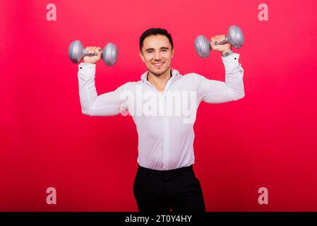 Geschäftsmann mit Fitness-Kurzhanteln trägt Hemd. Studioaufnahmen auf rotem Hintergrund Stockfoto