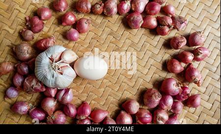 Foto von Gewürzen in Form von Schalotten, Knoblauch, Chilis und Eiern, die in einem gewebten Bambus angeordnet sind Stockfoto