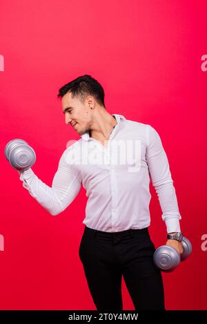 Geschäftsmann mit Fitness-Kurzhanteln trägt Hemd. Studioaufnahmen auf rotem Hintergrund Stockfoto