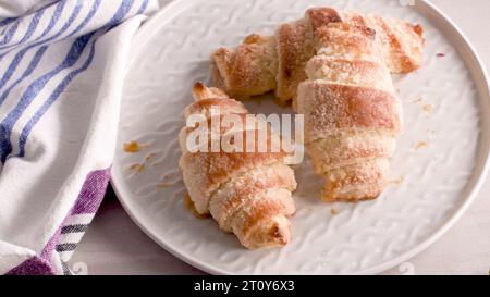 Kleine Croissants auf weißen Keramikplatten, hausgemachte Kuchen auf Betontischplatte. Stockfoto