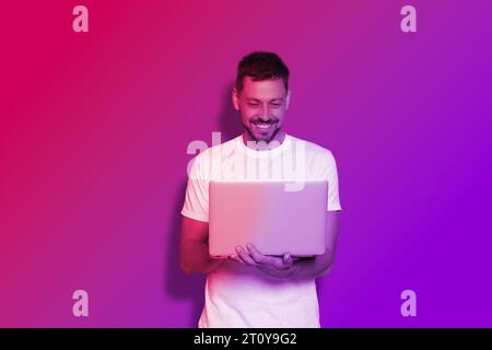 Schöner Mann mit Laptop in Neonlichtern Stockfoto