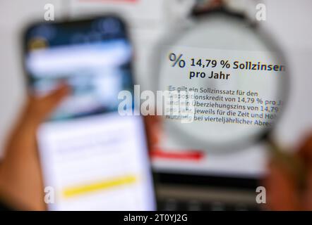 Leipzig, Deutschland. Oktober 2023. Durch eine Lupe sehen Sie die Worte „79 % Sollzinsen pro Jahr“ für eine Überziehungsfazilität bei einer Sparkasse. Die Verbraucherschutzminister der länder und des Bundes bestehen auf einer Obergrenze für Überziehungszinsen. Nach Ansicht der Stiftung Warentest sind Überziehungseinrichtungen zu teuer, wenn sie mehr als 15,25 Prozent Zinsen Kosten. Quelle: Jan Woitas/dpa/Alamy Live News Stockfoto