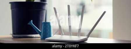 WLAN-Router mit Antennen steht in der Nähe einer üppigen Pflanze im Topf Stockfoto