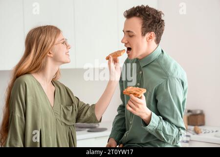 Junge Frau füttert ihren Freund mit leckerem Toast mit Nussbutter in der Küche Stockfoto